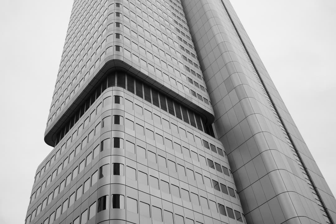 A low-angle view of a modern skyscraper with a grid of windows (Photo by Gabriel Hohenstein on Unsplash)